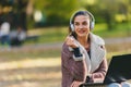 Portrait of beautiful young woman in the park using laptop computer listening over headphones studying outdoors in the nature Royalty Free Stock Photo