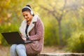 Portrait of beautiful young woman in the park using laptop computer listening over headphones studying outdoors in the nature Royalty Free Stock Photo