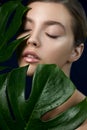 Portrait of beautiful young woman with perfect skin posing with closed eyes through the tropical green leaves Royalty Free Stock Photo