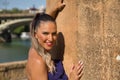 Portrait of beautiful young woman, with pigtail, wearing a purple dress, smiling and relaxed leaning against a stone wall. Concept Royalty Free Stock Photo