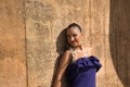 Portrait of beautiful young woman, with pigtail, wearing a purple dress, smiling and relaxed leaning against a stone wall. Concept Royalty Free Stock Photo