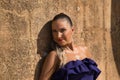 Portrait of beautiful young woman, with pigtail, wearing a purple dress, smiling and relaxed leaning against a stone wall. Concept Royalty Free Stock Photo