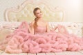 Portrait of beautiful young woman in pink dress posing in bedroom