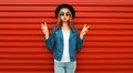 Portrait of beautiful young woman posing blowing her lips sending sweet air kiss wearing blue jacket and black round hat on red Royalty Free Stock Photo