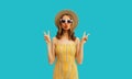 Portrait of beautiful young woman posing blowing her lips sending sweet air kiss wearing summer straw hat and dress on blue Royalty Free Stock Photo