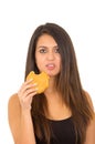 Portrait beautiful young woman posing for camera eating hamburger while making guilty facial expression, white studio