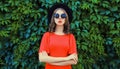 Portrait of beautiful young woman posing in red dress, black round hat on green leaves wall background Royalty Free Stock Photo