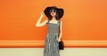 Portrait of beautiful young woman posing wearing black summer straw hat and striped dress on orange background Royalty Free Stock Photo