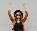 Beautiful young woman raising her hands up wearing a black round hat, brown jacket on a gray background Royalty Free Stock Photo