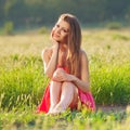 Portrait of a beautiful young woman in a red dress on a background of sky and grass in summer Royalty Free Stock Photo