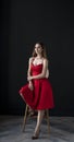 Portrait of a young woman in a red dress sitting on a high bar stool Royalty Free Stock Photo