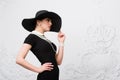 Portrait of a beautiful young woman in retro style in an elegant black hat and dress over luxury rococco wall background Royalty Free Stock Photo