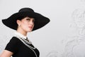 Portrait of a beautiful young woman in retro style in an elegant black hat and dress over luxury rococco wall background Royalty Free Stock Photo