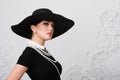 Portrait of a beautiful young woman in retro style in an elegant black hat and dress over luxury rococco wall background Royalty Free Stock Photo