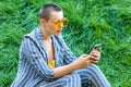 Portrait of beautiful young woman with short hair in casual blue striped suit, yellow glasses sitting on green grass holding her Royalty Free Stock Photo