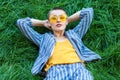 Portrait of beautiful young woman with short hair in casual blue striped suit, yellow shirt, glasses lying down on green grass, Royalty Free Stock Photo