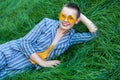 Portrait of beautiful young woman with short hair in casual blue striped suit, yellow shirt and glasses lying down on green grass Royalty Free Stock Photo