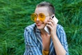 Portrait of beautiful young woman with short hair in casual blue striped suit, yellow shirt and glasses sitting on green grass on Royalty Free Stock Photo