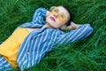 Portrait of beautiful young woman with short hair in casual striped suit, yellow shirt, glasses lying down on green grass, resting Royalty Free Stock Photo