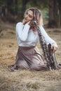 Portrait of a beautiful young woman sitting on the dry grass leanher head on saxophone, romantic blonde girl close eyes and Royalty Free Stock Photo
