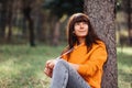 Portrait of a beautiful young woman sitting in the grass by a tree and posing. Recreation at the park Royalty Free Stock Photo