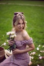 portrait of a beautiful young woman sitting on a green meadow in summer and holding a bouquet of pions. Royalty Free Stock Photo