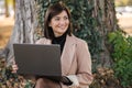 Portrait of beautiful young woman sitting in the park with laptop and working. Female smiling. Place for text Royalty Free Stock Photo