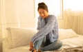 Portrait of beautiful young woman smiling friendly in knitted sweater enjoying sunny evening while sitting on bed in bedroom. Royalty Free Stock Photo