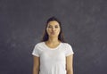 Beautiful young woman standing on gray background with folded lips in anticipation of kiss.