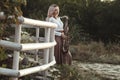 Portrait of a beautiful young woman standing and leaninf on wooden white fence with saxophone, romantic blonde girl relaxing on Royalty Free Stock Photo