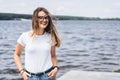 Portrait of a beautiful young woman in stylish glasses. Girl in white tshirt posing on the background of the lake landscape Royalty Free Stock Photo