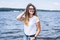 Portrait of a beautiful young woman in stylish glasses. Girl in white tshirt posing on the background of the lake landscape Royalty Free Stock Photo