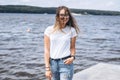 Portrait of a beautiful young woman in stylish glasses. Girl in white tshirt posing on the background of the lake landscape Royalty Free Stock Photo