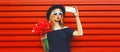 Portrait of beautiful young woman taking selfie with smartphone holding bouquet of pink rose flowers in black round hat on red