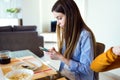 Beautiful young woman using her mobile phone while having lunch with friends at home. Royalty Free Stock Photo