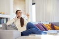 Lovely young woman talking with somebody on her mobile phone while sitting on sofa at home Royalty Free Stock Photo