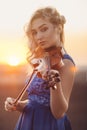 Portrait of a beautiful young woman with a violin under her chin at sunset, girl playing a musical instrument on nature, concept