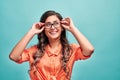 Portrait of a beautiful young woman wearing an orange shirt and glasses stands on a blue background and looks up.Copy space Royalty Free Stock Photo