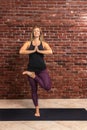 Portrait of beautiful young woman wearing sportswear working out against brick wall, doing yoga or pilates exercise. Standing in Royalty Free Stock Photo