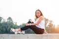 Portrait of beautiful young woman in white t-shirt and black trousers sitting in nature at sunset