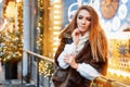 Portrait of a beautiful young woman who poses on the street near the elegantly decorated Christmas window, festive mood Royalty Free Stock Photo