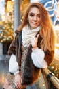 Portrait of a beautiful young woman who poses on the street near the elegantly decorated Christmas window, festive mood Royalty Free Stock Photo