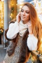 Portrait of a beautiful young woman who poses on the street near the elegantly decorated Christmas window, festive mood Royalty Free Stock Photo