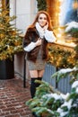 Portrait of a beautiful young woman who poses on the street near the elegantly decorated Christmas window, festive mood Royalty Free Stock Photo
