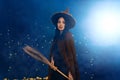 Portrait of beautiful young woman in witch halloween costume wear witches hat holding broom over spooky dark magic background - Royalty Free Stock Photo