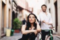 Portrait of a beautiful young woman. A woman in a black dress sat on a chair. A man behind her stands with a green bike Royalty Free Stock Photo