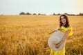 Portrait of a beautiful young woman in a yellow dress on a golden wheat field at sunset. The girl holds a large straw hat in her Royalty Free Stock Photo