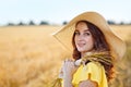 Portrait of a beautiful young woman in a yellow dress and a straw hat on a golden wheat field at sunset. A sensual girl enjoys Royalty Free Stock Photo