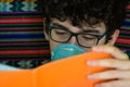 Portrait of a bedridden caucasian boy wearing a blue protective mask. He is studying his orange-covered notebook. Home study