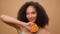 Portrait in beige background advertise female girl African American woman hold half of orange citrus vitamin pampering